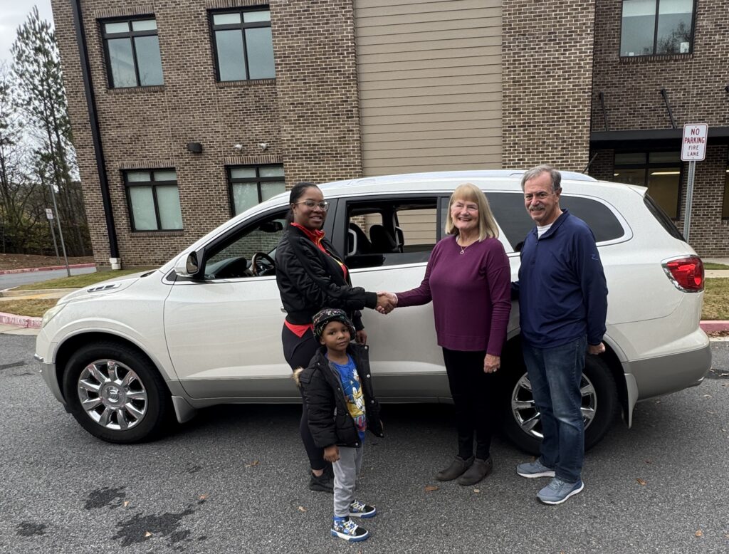 car donors shake hands with recipient while standing in front of the white SUV